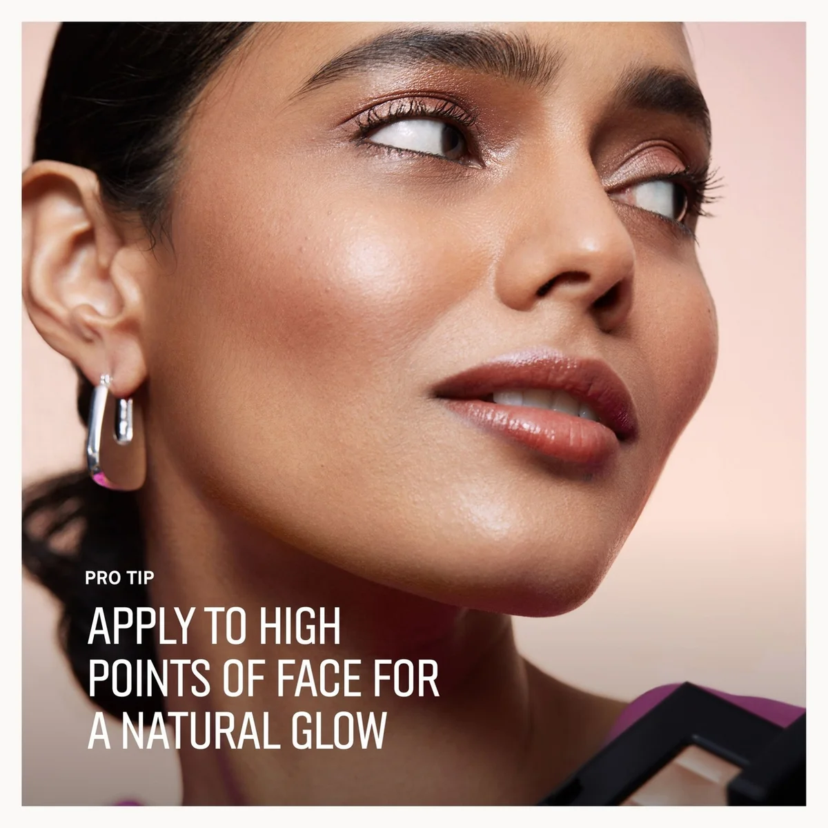 A close-up beauty tip graphic showing part of a woman's face wearing silver hoop earrings, with text that reads 'PRO TIP APPLY TO HIGH POINTS OF FACE FOR A NATURAL GLOW' on a soft peach background.