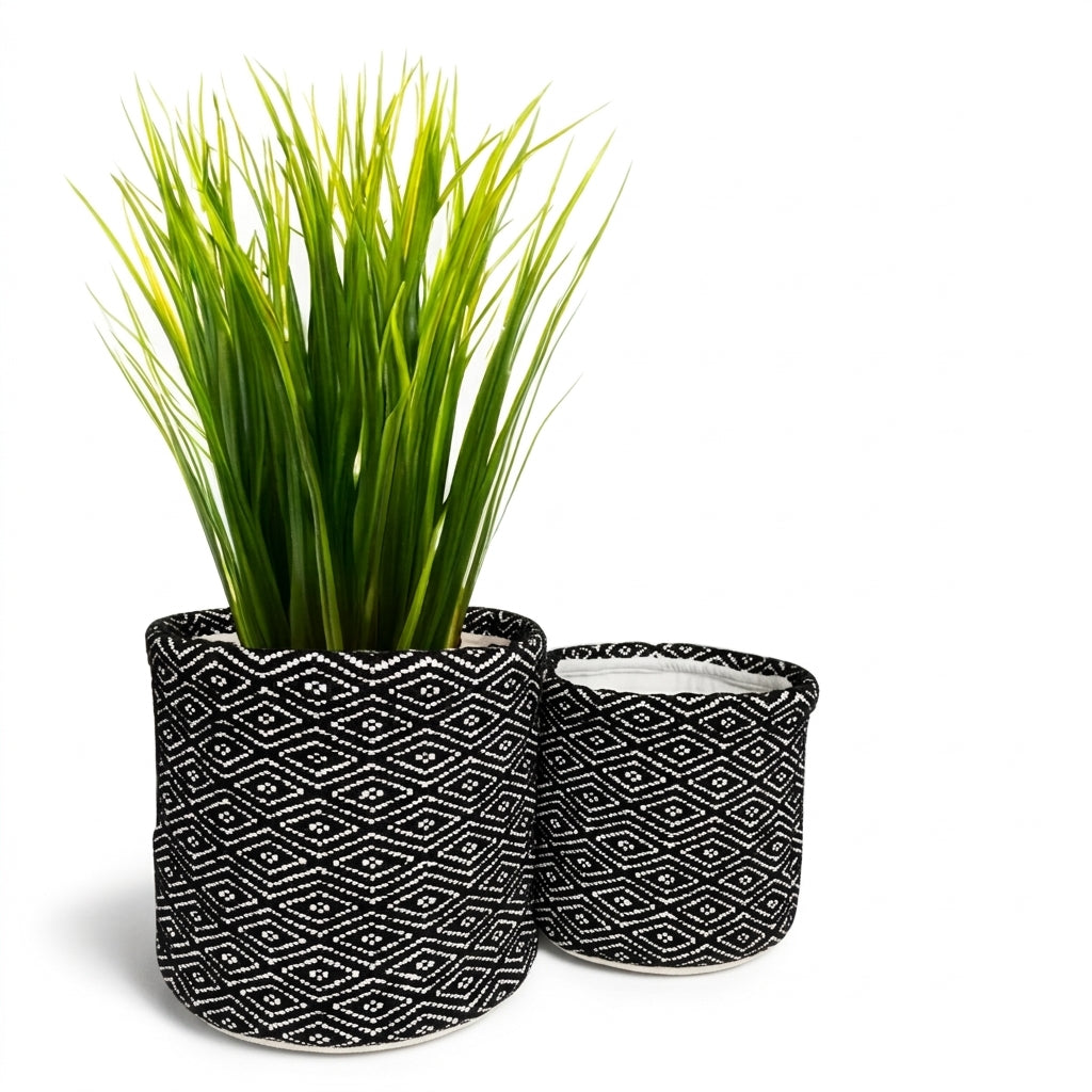 Two cylindrical planters with a black and white geometric diamond pattern, one larger planter holding bright green artificial grass and one smaller matching planter, shown on a white background.