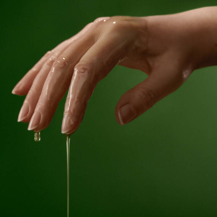 Hand with a drop of oil on a green background
