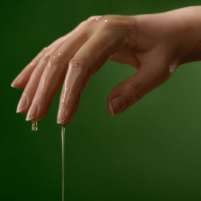 Hand with a drop of oil on a green background