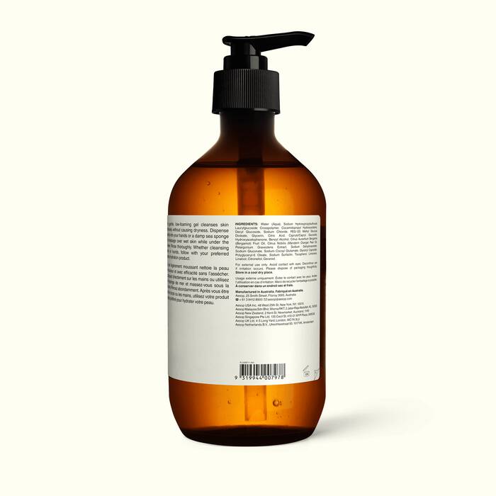 An amber glass pump Aesop-Geranium-Leaf-Body-Cleanser bottle with a black dispenser and a white back label, photographed against a plain off-white background.