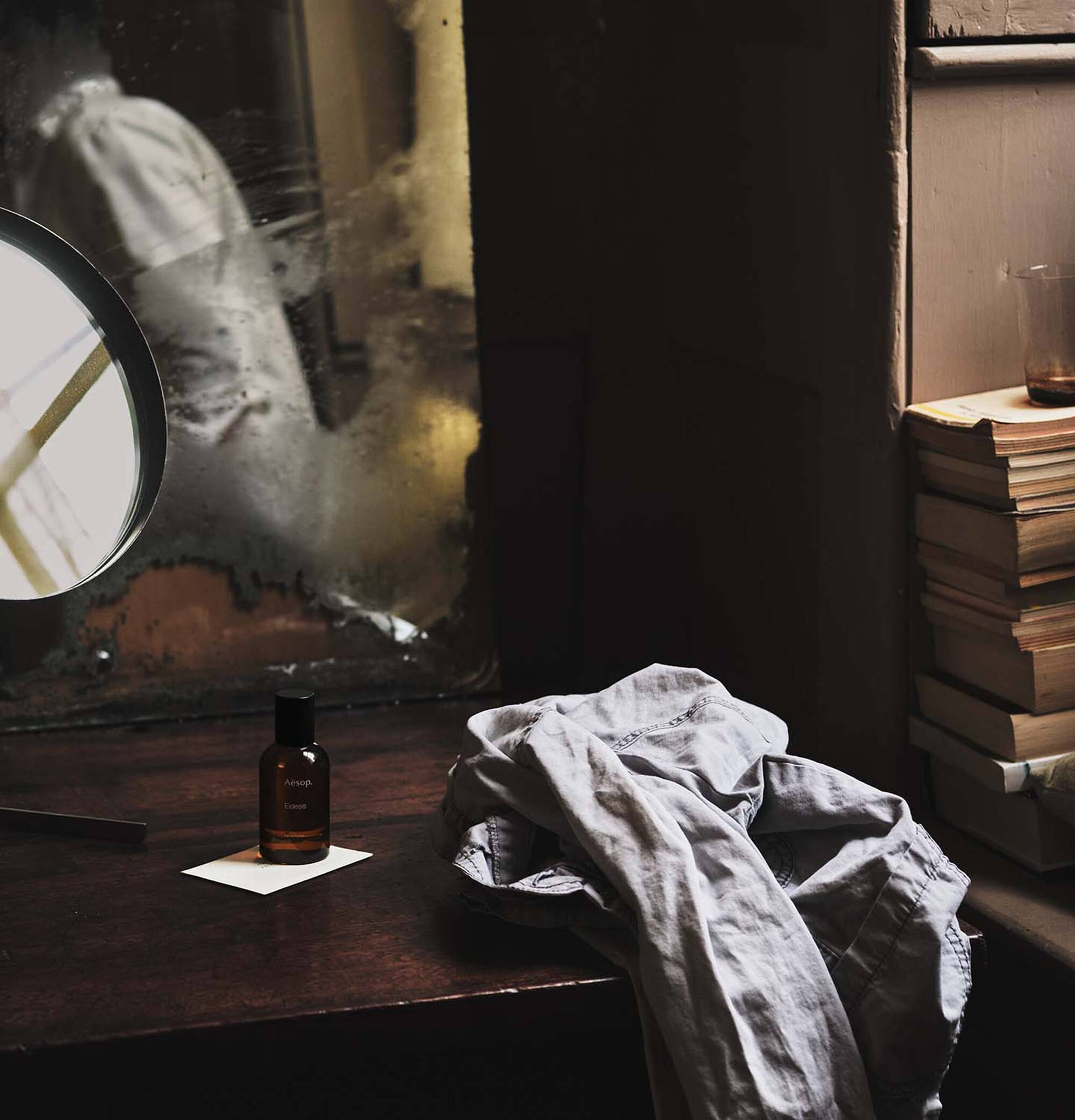 Vintage-style room with books, a bottle of Aesop Eidesis Eau de Parfum, and a cloth on a table.