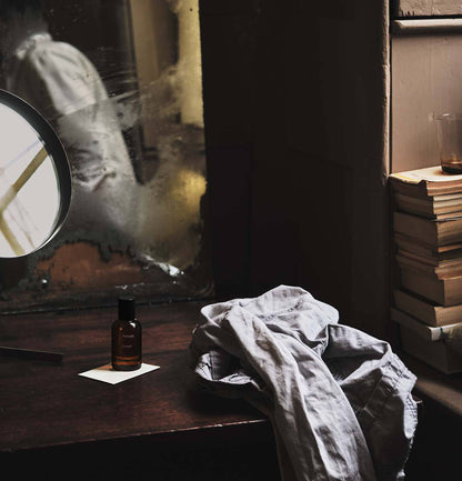 Vintage-style room with books, a bottle of Aesop Eidesis Eau de Parfum, and a cloth on a table.