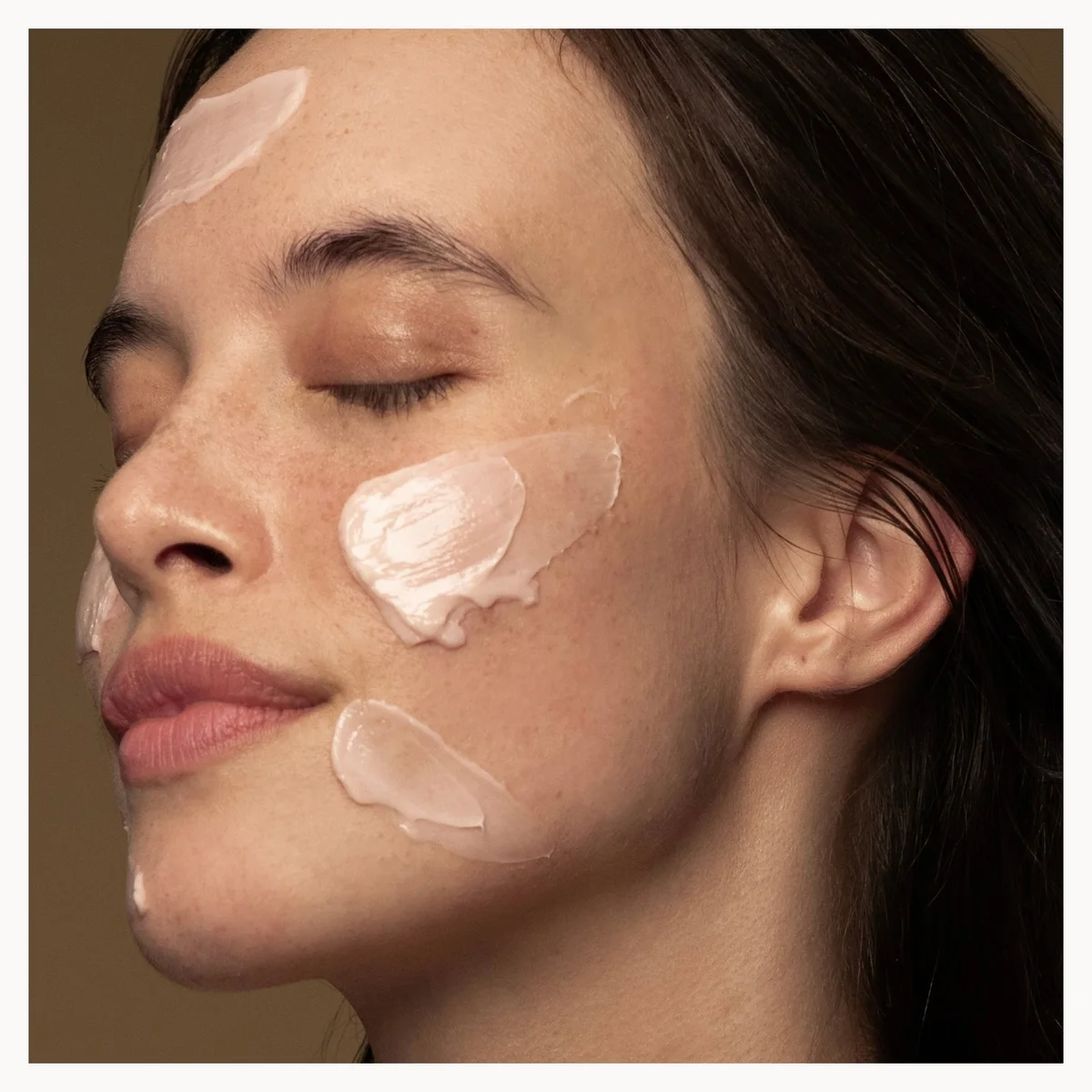 Close-up of a woman's face with cosmetic cream applied to her cheeks.