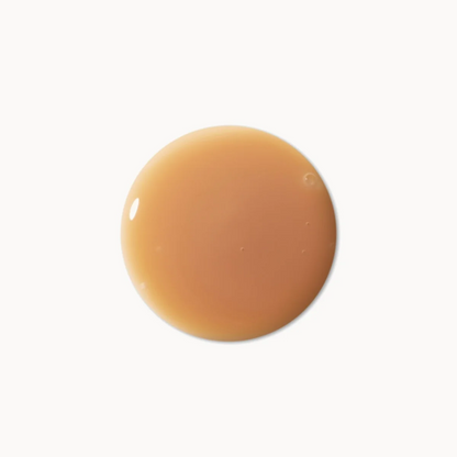 A glossy, smooth circular swatch of warm caramel or tan cosmetic cream on a solid white background.