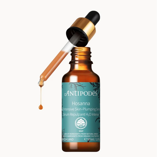An amber glass dropper bottle of Antipodes Cosmetics Hosanna serum with a teal label, shown with the dropper tilted to release a single drop of liquid against a plain white background.