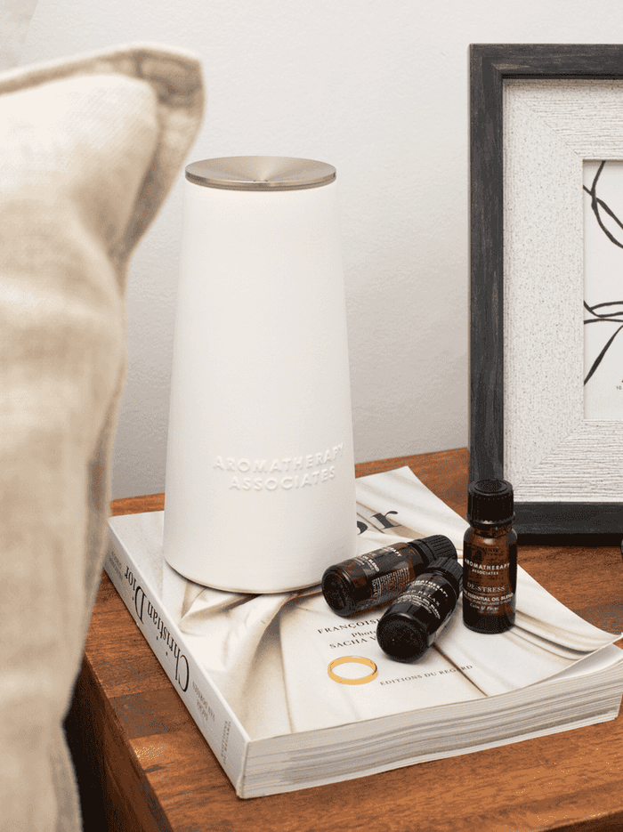 White diffuser on a stack of books with essential oil bottles on a wooden surface.