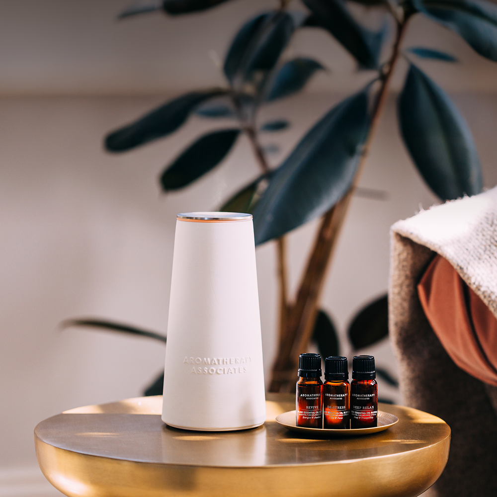 White diffuser and essential oil bottles on a gold tray with a plant in the background