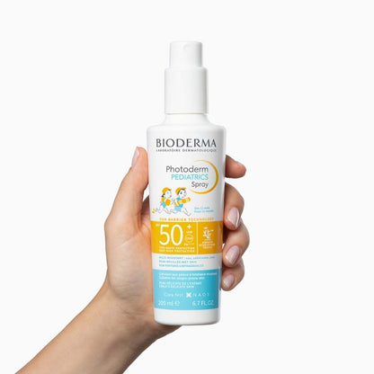 Bioderma kids sunscreen spray held in a hand against a white background