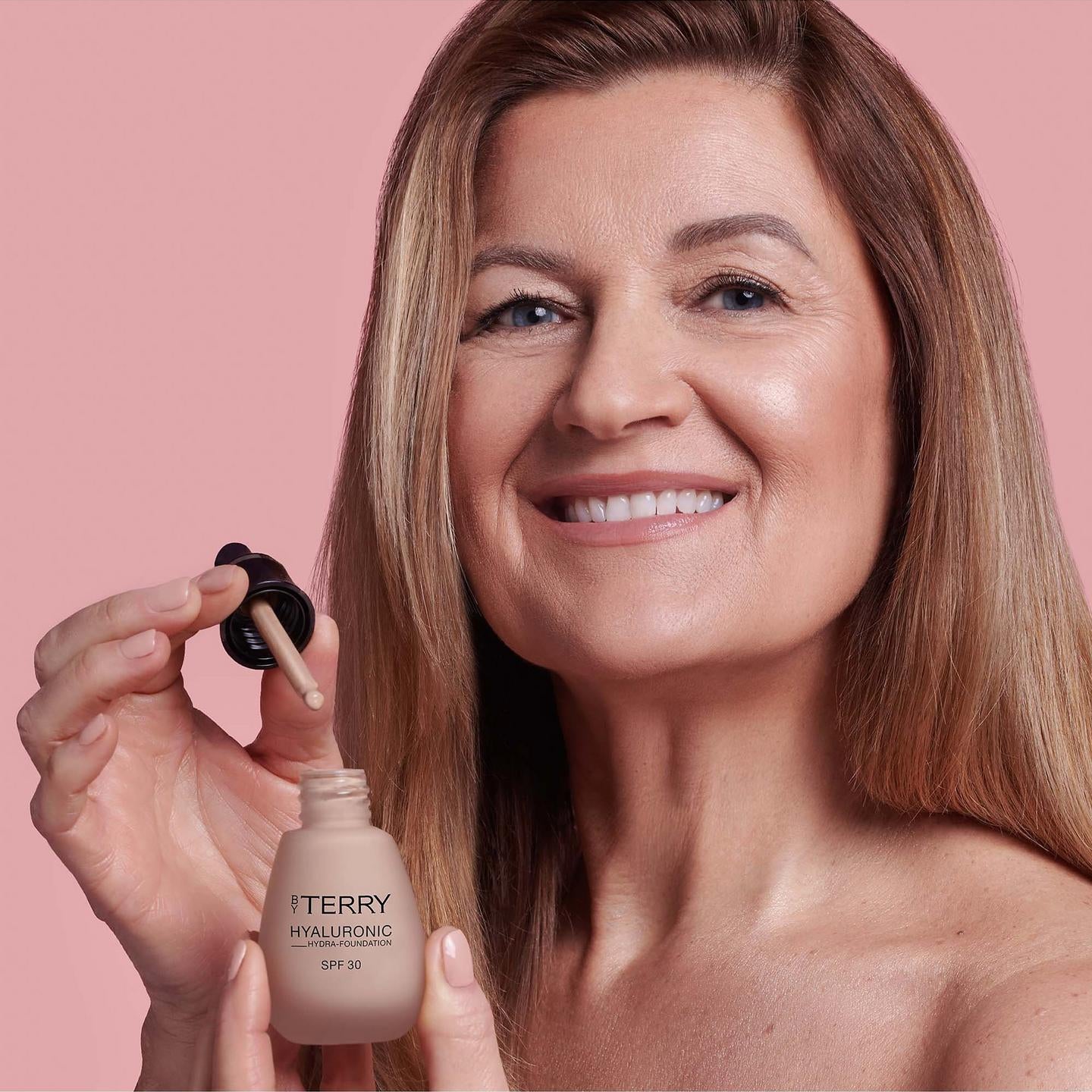Woman holding a bottle of Iteryn foundation with a pink background