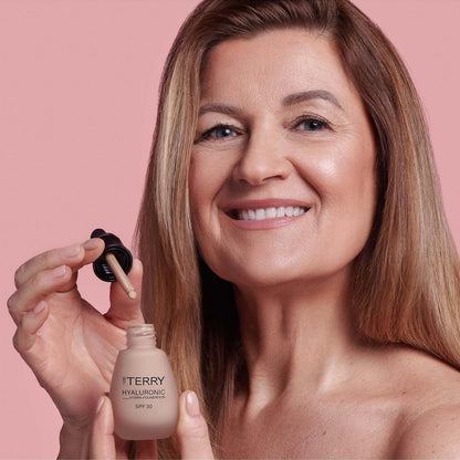 Woman holding a bottle of Iteryn foundation with a pink background