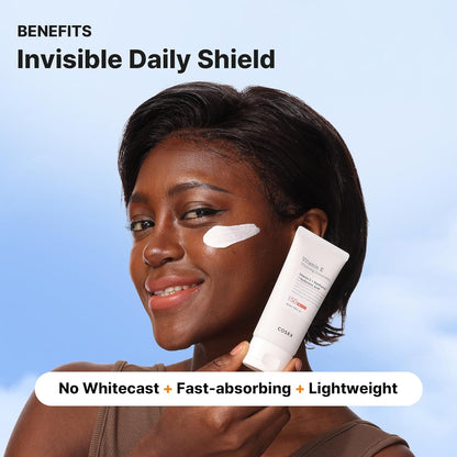 Woman applying sunscreen with a tube labeled 'Invisible Daily Shield' against a blue sky background.