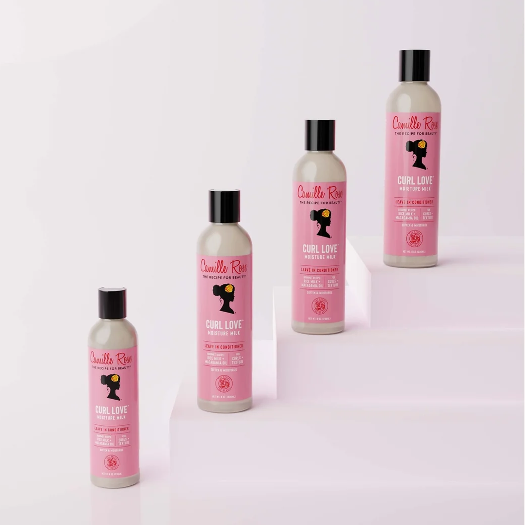 Four bottles of Curly Girl Deva Curl Love Curl Cream in a gradient pink and white design, arranged on white steps against a light pink background.