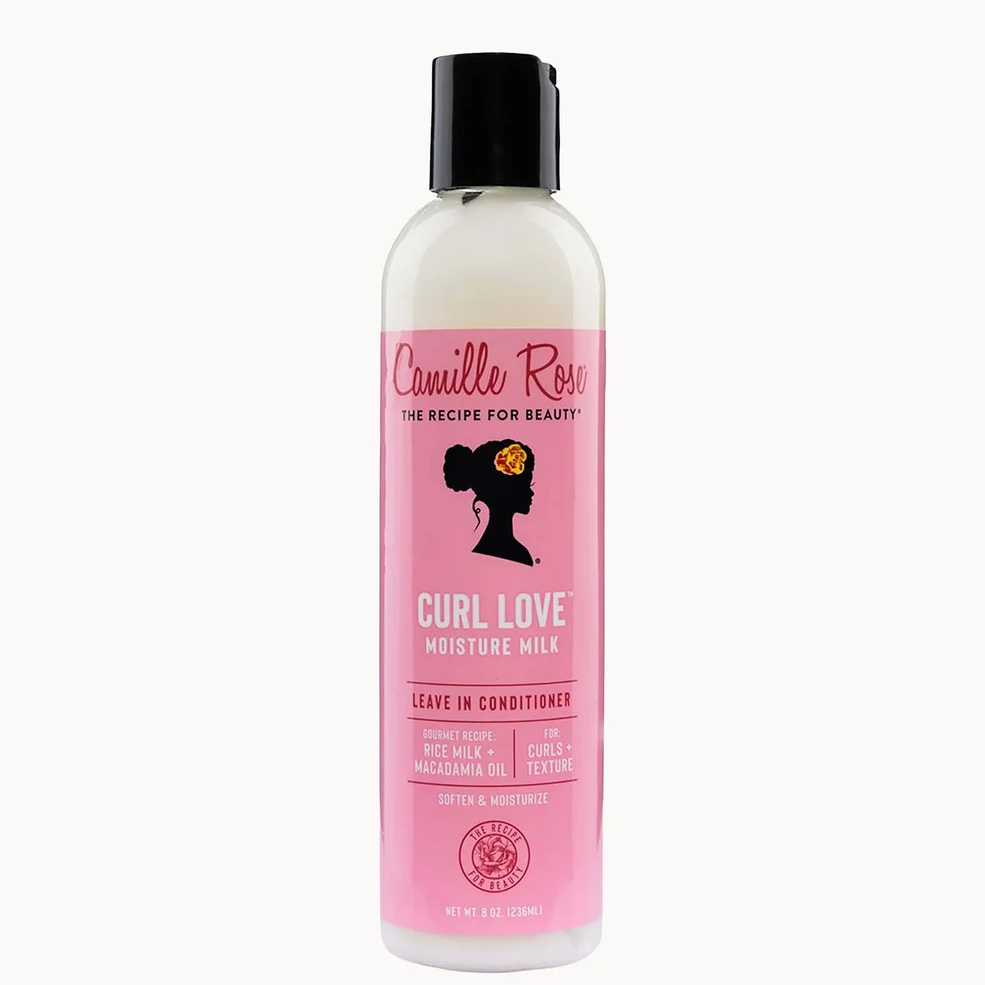 A bottle of Camille Rose Curl Love Moisture Milk leave-in conditioner, featuring a pink label and black cap on a light off-white background.