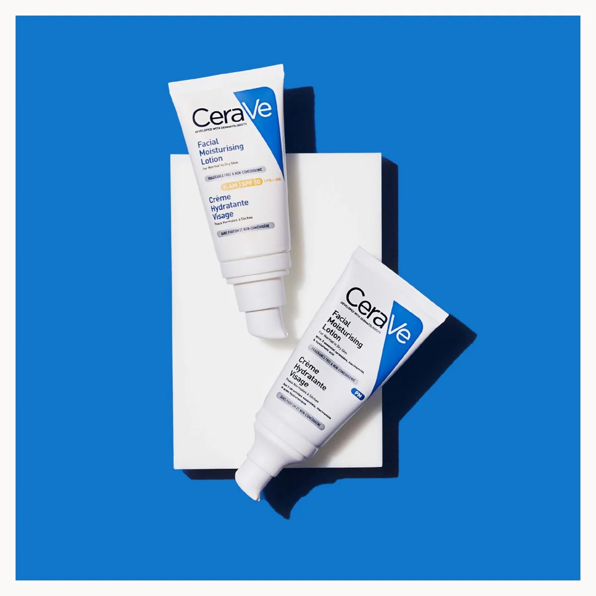 Two CeraVe skincare tubes, a Facial Moisturizing Cream and a Serum, arranged diagonally on a white rectangular block against a solid blue background.
