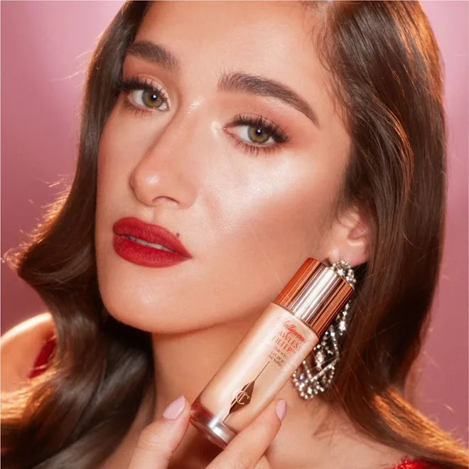 Woman holding a makeup product with a pink background