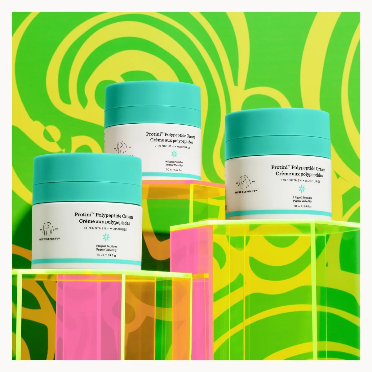 Three jars of Protein Polypeptide Cream arranged on translucent acrylic pedestals against a bright green and yellow abstract patterned background.