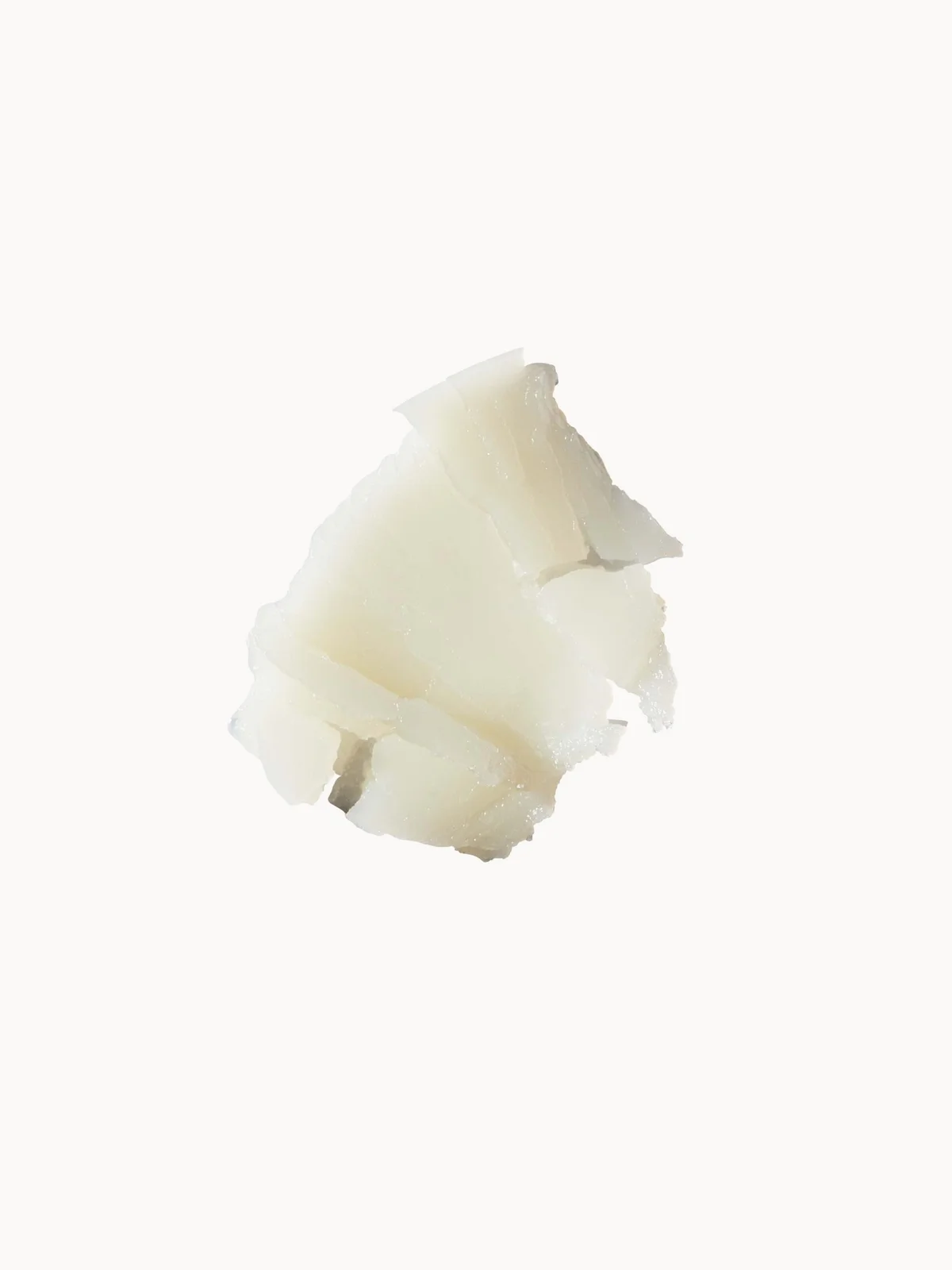 A small irregular piece of off-white wax or solid cosmetic material on a plain white background.
