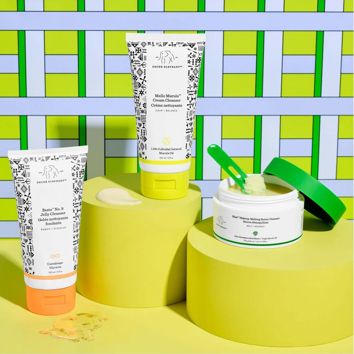 Three skincare products from Dr. Géréy's Beauty Bar are displayed on yellow pedestals against a green and blue patterned background.