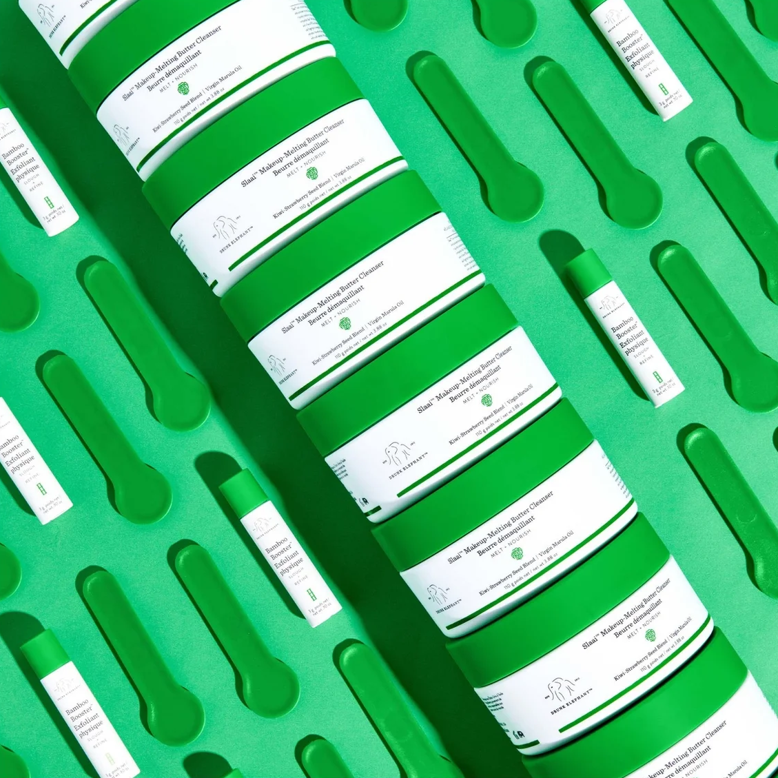 A set of green cosmetic jars with white labels arranged diagonally on a matching green tray with cutout compartments, alongside small green and white tubes.