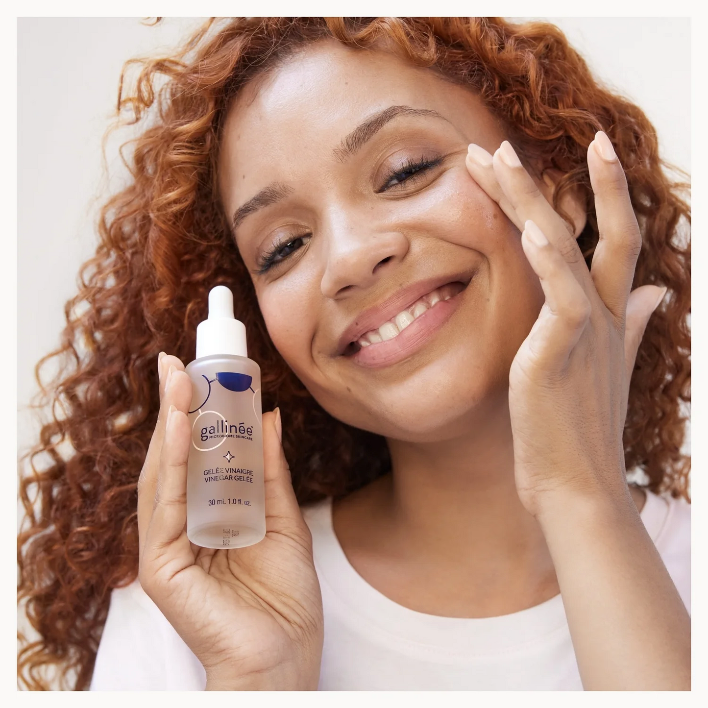 Woman holding a bottle of gallinee skincare product with a white background