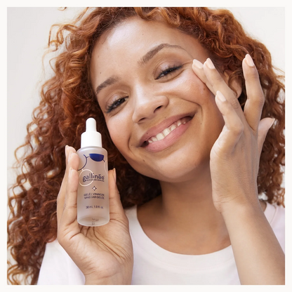 Woman holding a bottle of gallinee skincare product with a white background