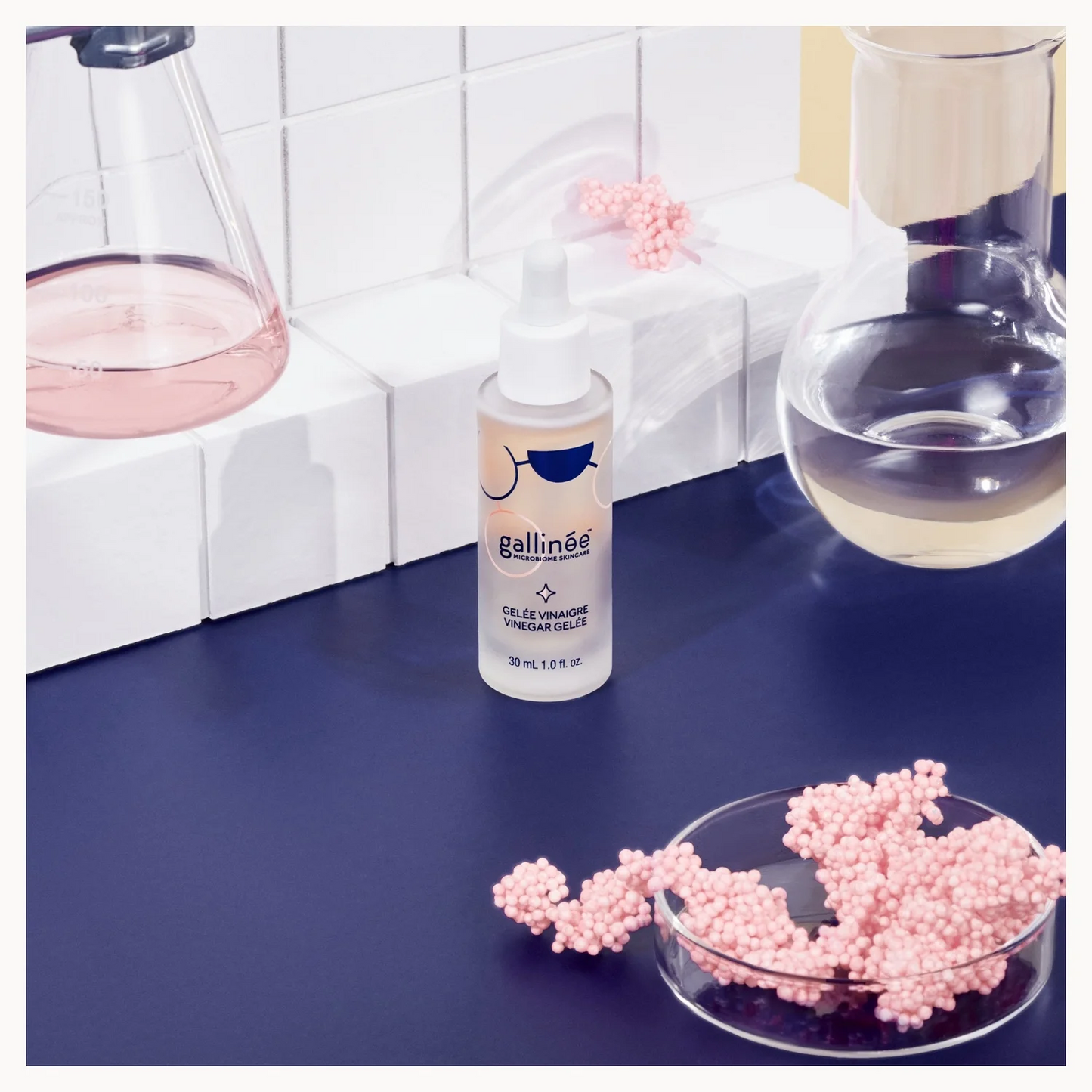 Bottle of galline product on a blue surface with pink beads and a white tiled wall background.