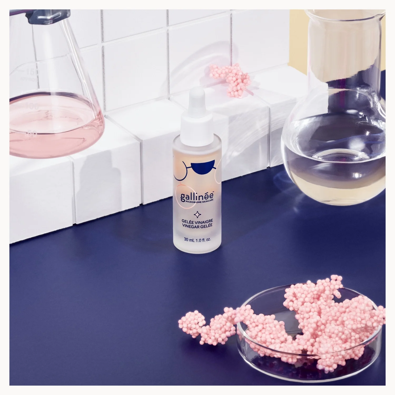 Bottle of galline product on a blue surface with pink beads and a white tiled wall background.