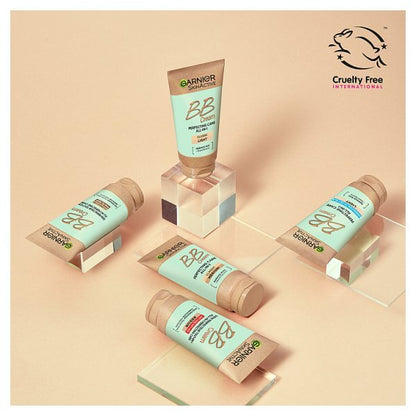 Four tubes of Garnier Instant BB Cream displayed on clear acrylic blocks against a warm beige background, with the Cruelty Free International logo in the top right corner.