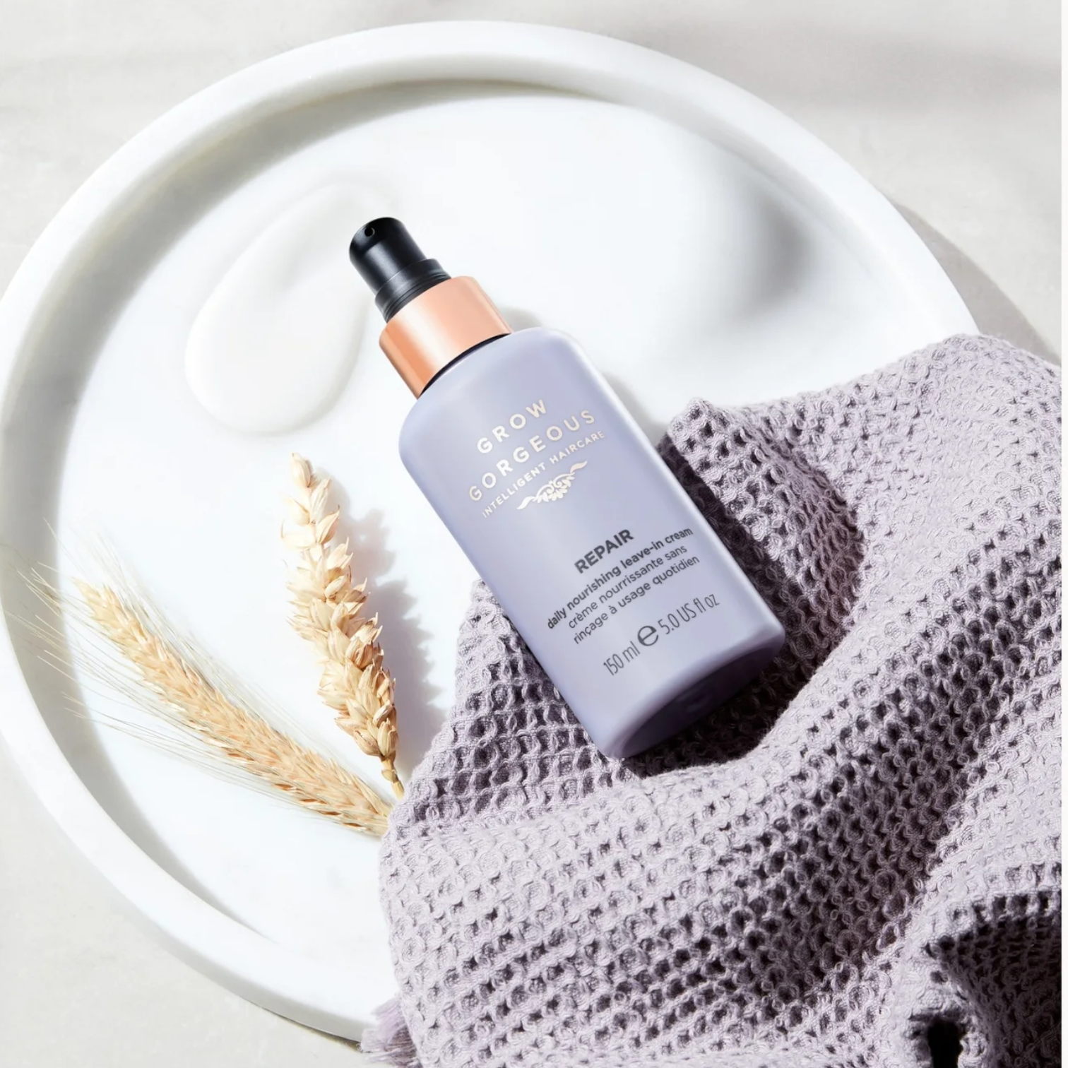 Haircare bottle labeled 'Glow' on a textured surface with a white plate and dried plant elements.