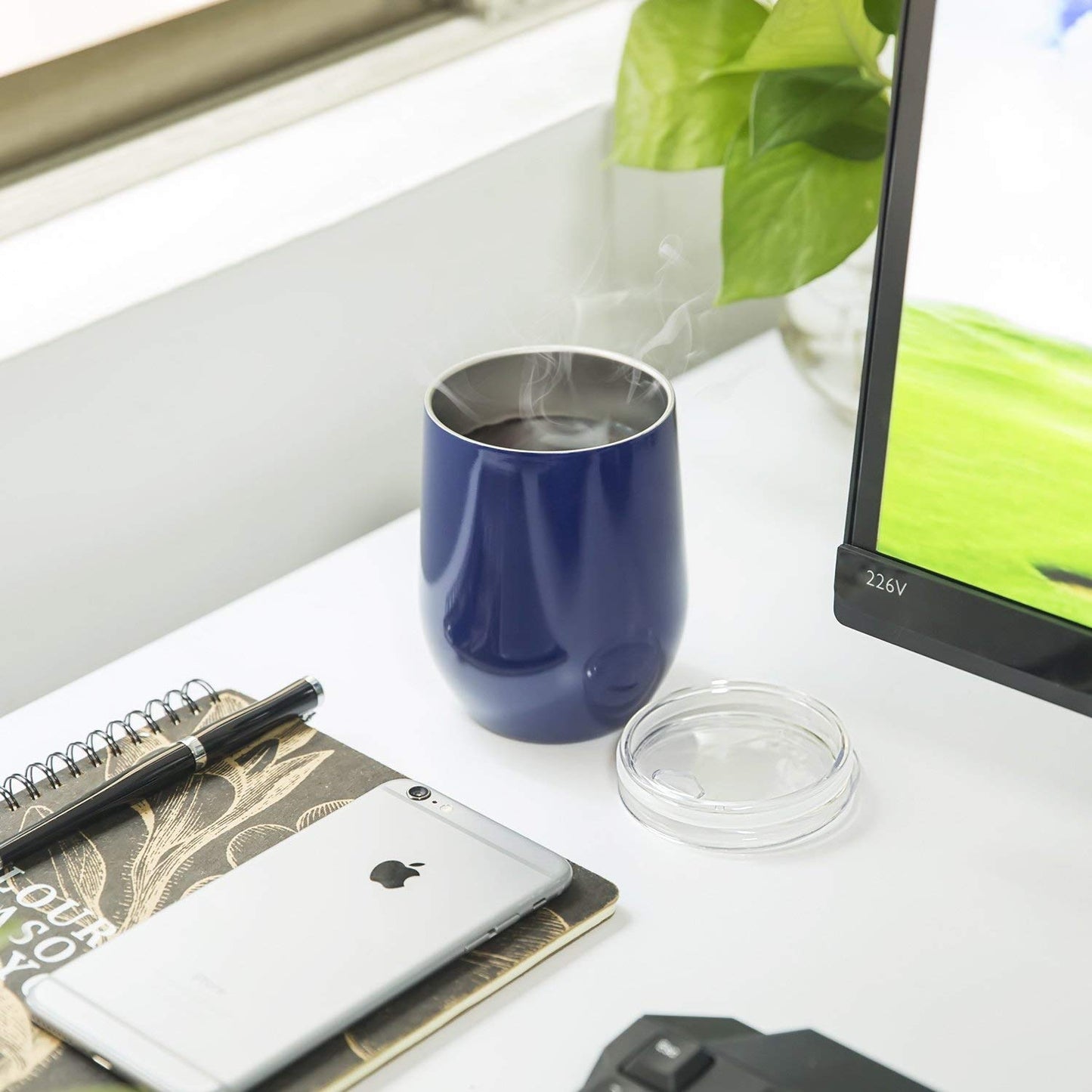Blue mug with steam, smartphone, notebook, pen, and computer on a desk.