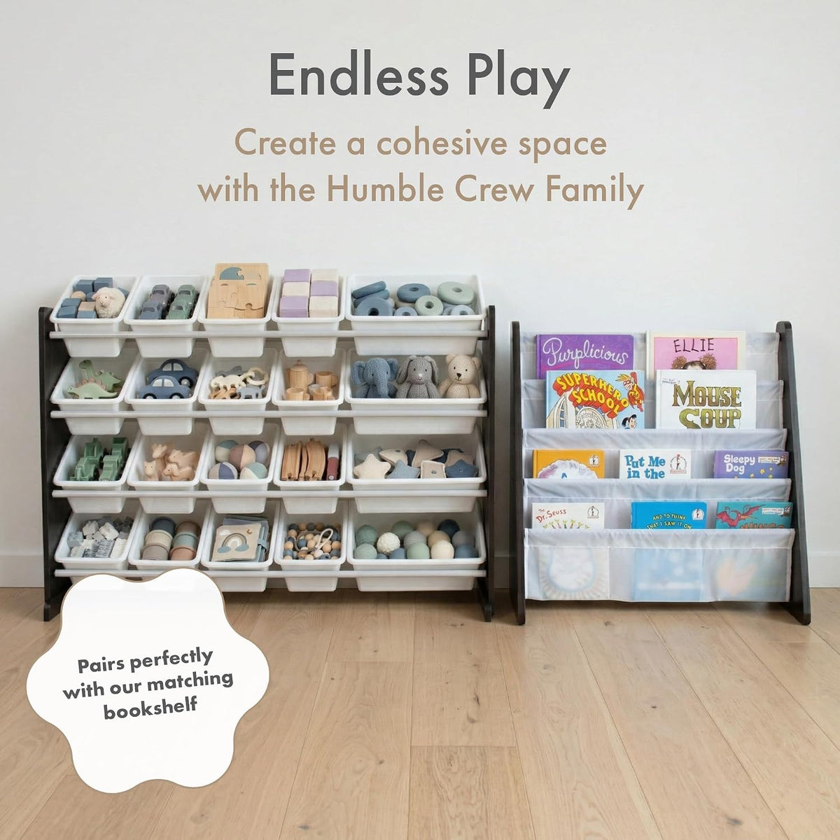 A children's storage organizer set in a nursery-like room, featuring a tall white plastic bin rack filled with toys on the left and a matching dark bookshelf with clear bins holding children's books on the right. Text at the top reads 'Endless Play' and 'Create a cohesive space with the Humble Crew Family,' with a cloud badge saying 'Pairs perfectly with our matching bookshelf.