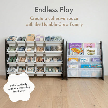 A children's storage organizer set in a nursery-like room, featuring a tall white plastic bin rack filled with toys on the left and a matching dark bookshelf with clear bins holding children's books on the right. Text at the top reads 'Endless Play' and 'Create a cohesive space with the Humble Crew Family,' with a cloud badge saying 'Pairs perfectly with our matching bookshelf.