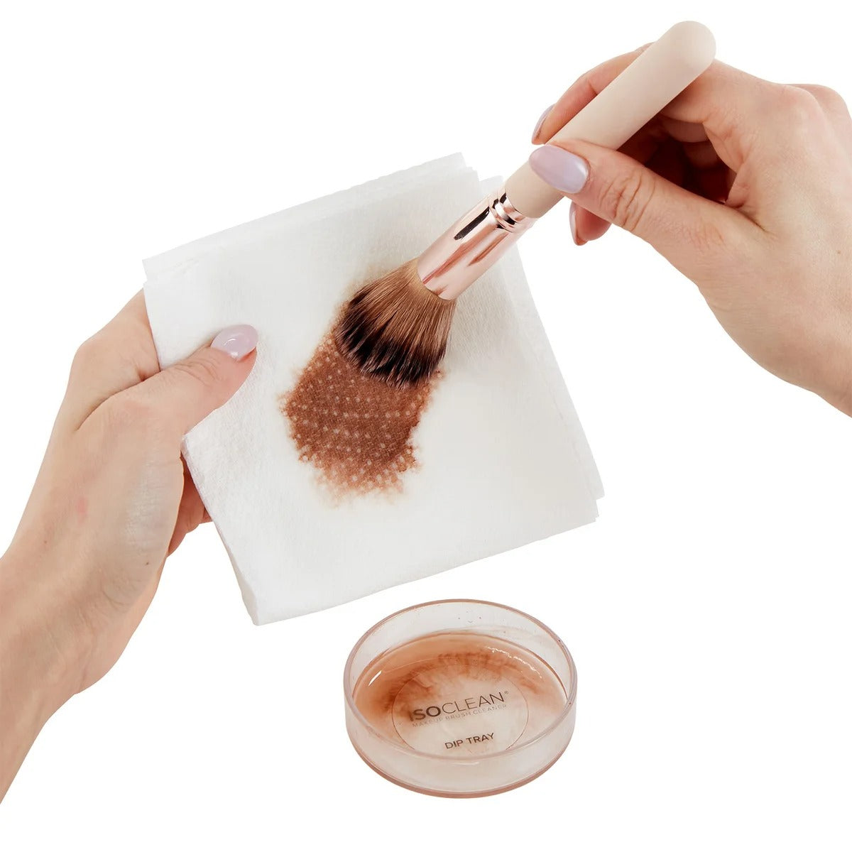 Person cleaning a makeup brush with a white pad and a container labeled 'ISO CLEAN' on a white background.