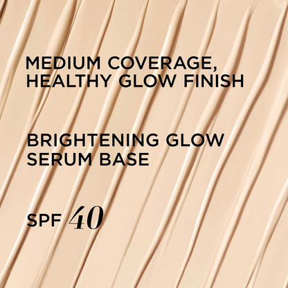 A close-up of a beige cosmetic serum base swatch with diagonal textured streaks and black text reading 'MEDIUM COVERAGE, HEALTHY GLOW FINISH', 'BRIGHTENING GLOW SERUM BASE', and 'SPF 40'.