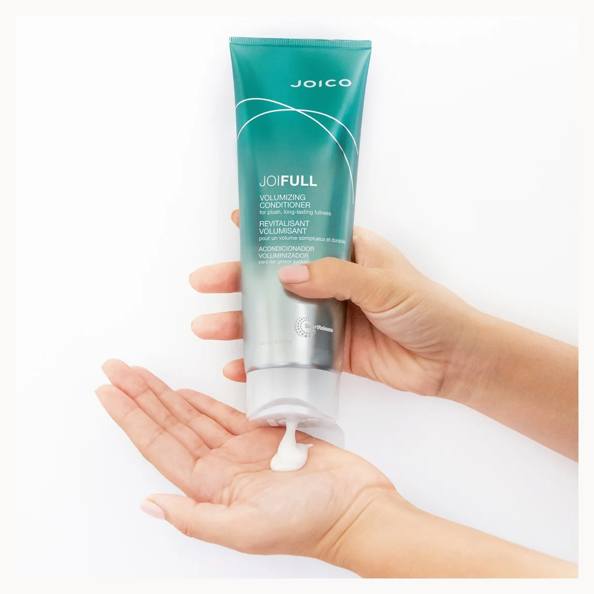 A person's hands holding a squeeze tube of Joico Joifull Volumizing Conditioner, with white cream being dispensed onto an open palm against a clean white background.