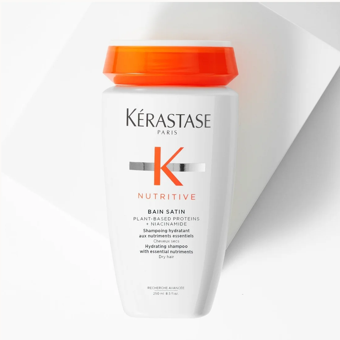 A white bottle of Kérastase Paris Bain 24/74 Nutritive shampoo with a bright orange cap, set against a clean white background with a diagonal shadow.