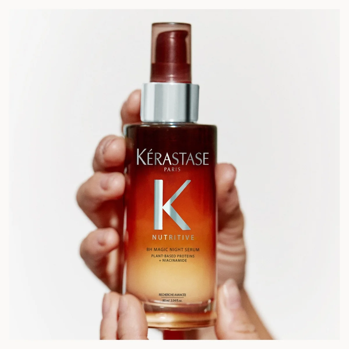 A hand holding a bottle of Kérastase Paris Nutritive No. 4 Hair Growth Serum against a plain white background.