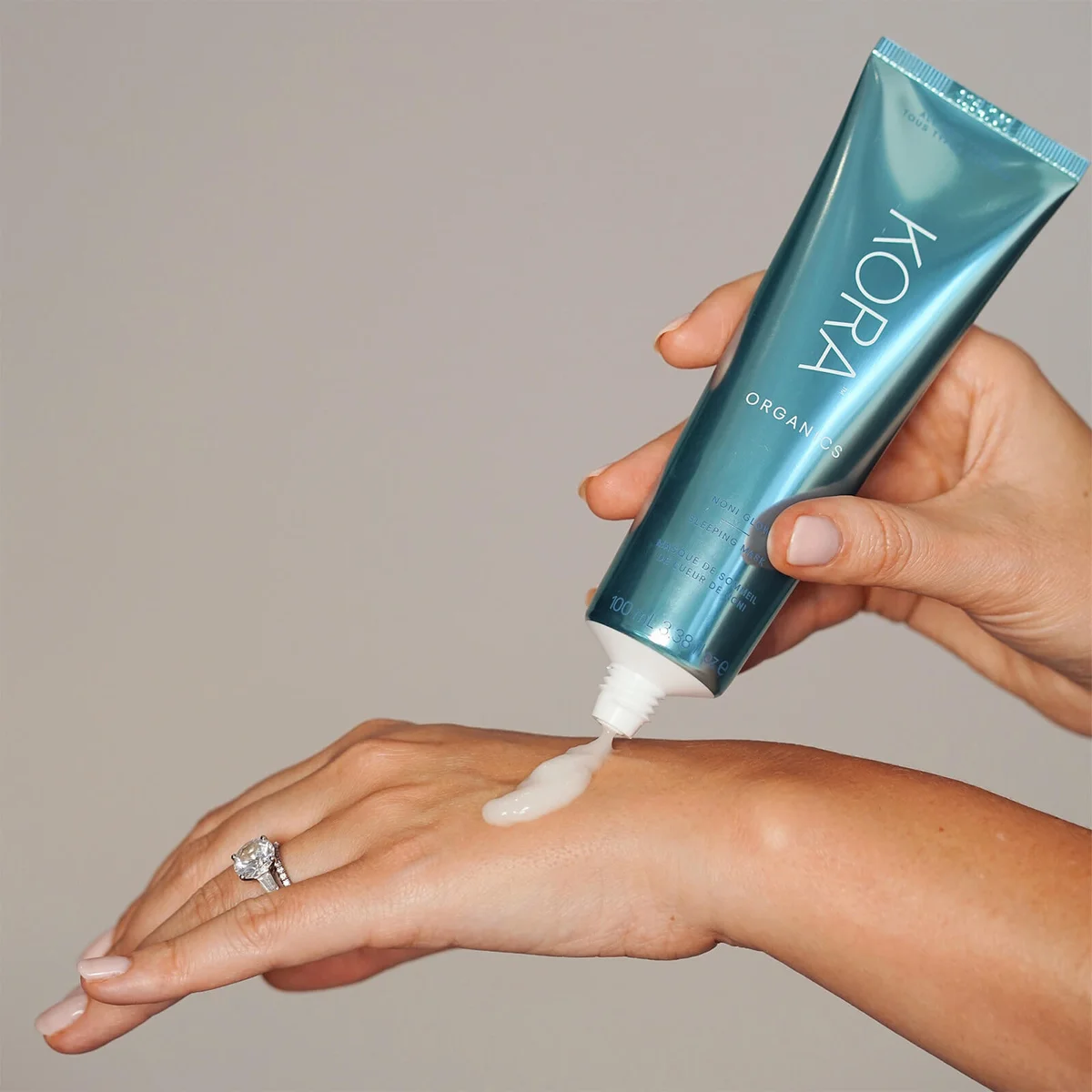 Hand applying Kora Organics product to wrist against a neutral background