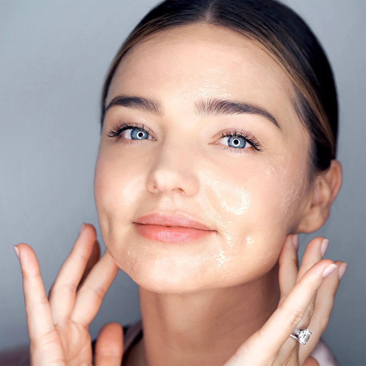 Model and founder Amanda Kerr  applying a skincare product to her face against a gray background