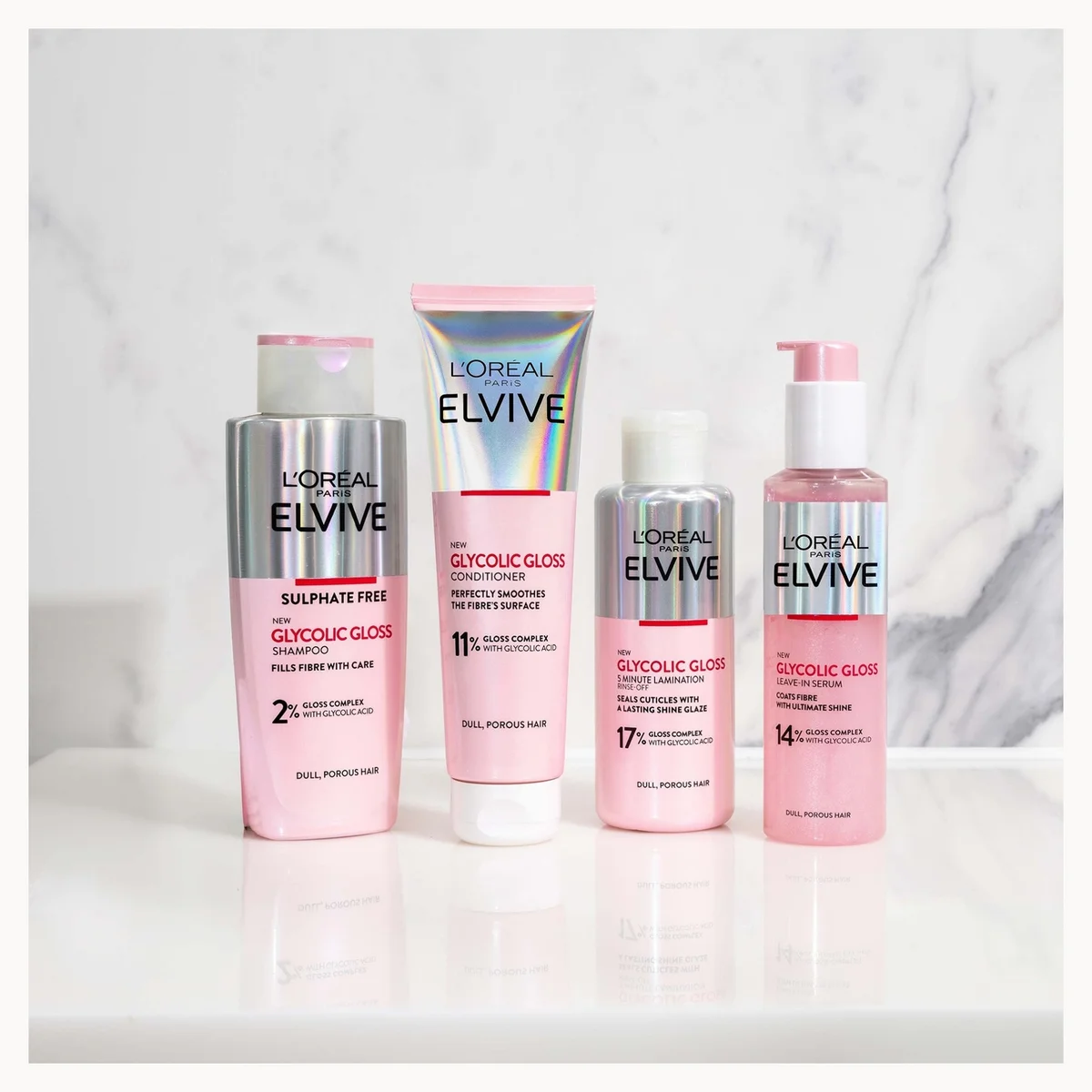 Four L'Orélés Elvive hair care products in pink packaging arranged on a white marble surface against a light marble background.