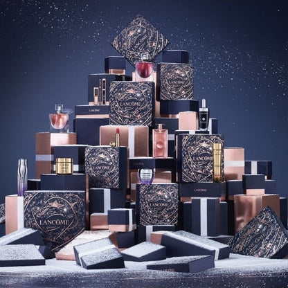 A luxury cosmetic gift set arranged in a pyramid stack, featuring multiple black and rose gold Lancôme boxes, bottles, and jars on a snowy surface against a dark blue background.
