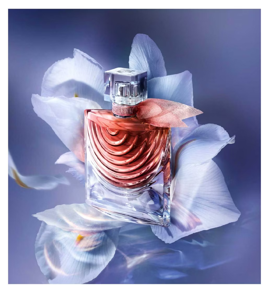 Perfume bottle with pink liquid on white petals against a blue background