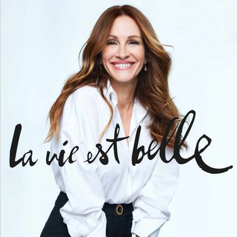 Actress Julia Roberts wearing a white shirt with 'La vie est belle' text on a light gray background