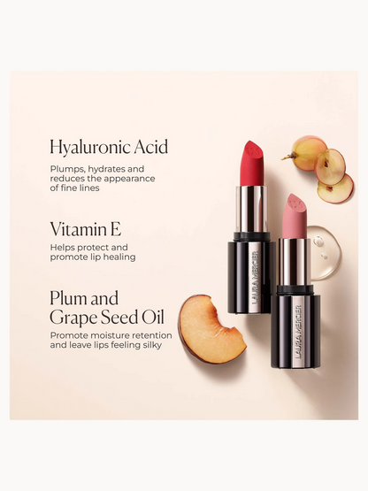 Two Laura Mercier lipsticks, one red and one pink, displayed on a light beige background with text describing key ingredients: Hyaluronic Acid, Vitamin E, and Plum and Grape Seed Oil. Sliced peaches and a small round cosmetic dish are styled as props.