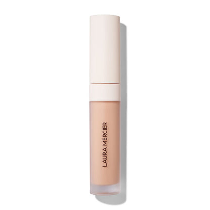 Laura Mercier liquid concealer in a clear tube showing the beige liquid formula, with a light beige cap, on a white background.
