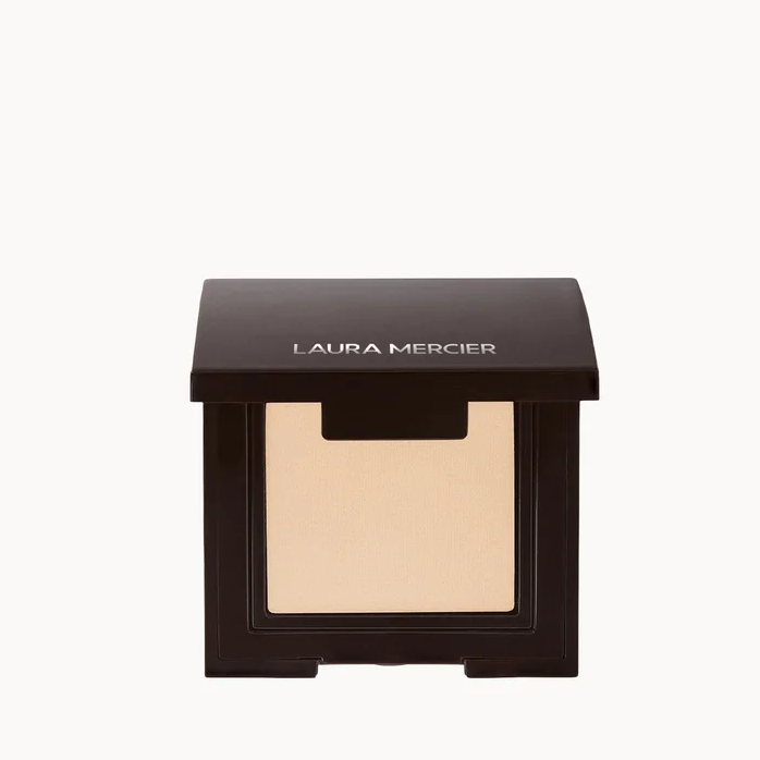 Laura Mercier eyeshadow compact in a dark brown square case with a clear window showing the beige eyeshadow powder inside, set against a plain white background.
