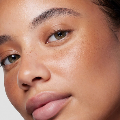 Close-up of a person's face showing natural skin texture and freckles, with a neutral studio background.