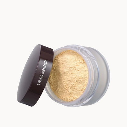 Laura Mercier loose face powder in a clear jar with its dark brown lid leaning against it, set against a solid off-white background.