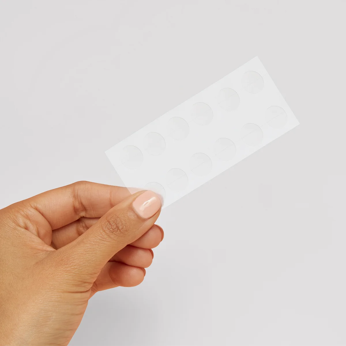 Hand holding a white square piece of paper with Invisible, anti-blemish face patches against a light gray background